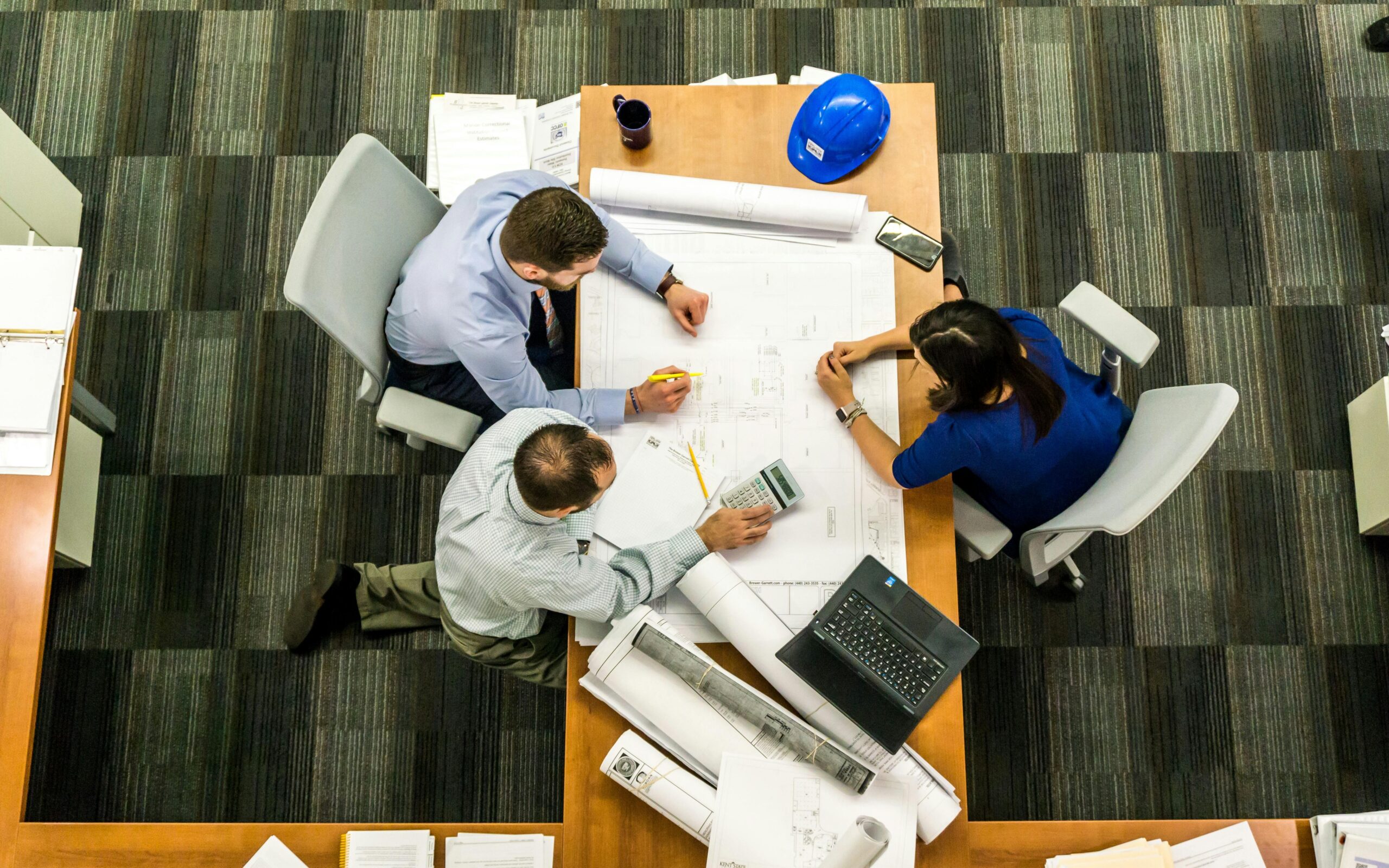 Project Management Courses Top view of a team working on construction plans in an office setting.