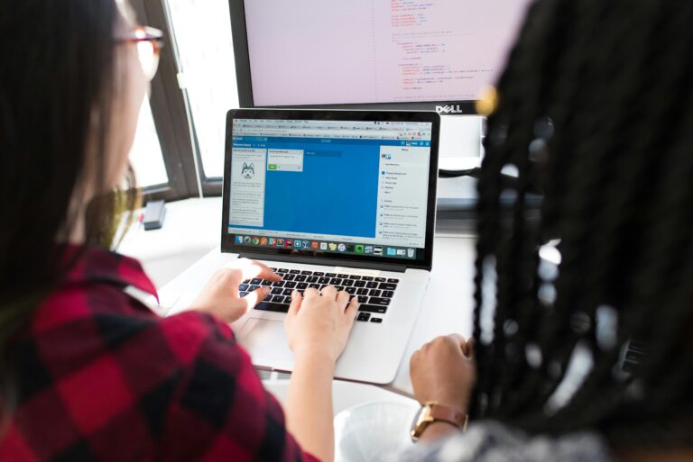 CAPM® Two women working together on a laptop in a bright, modern office setting.