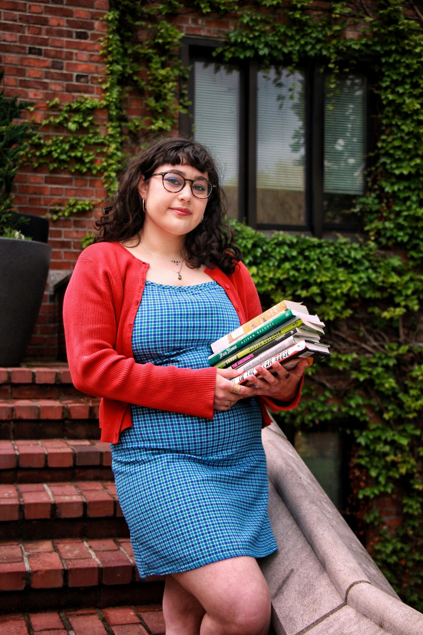 Agile & Scrum Certifications Young woman in casual attire holding books on outdoor brick staircase with ivy.