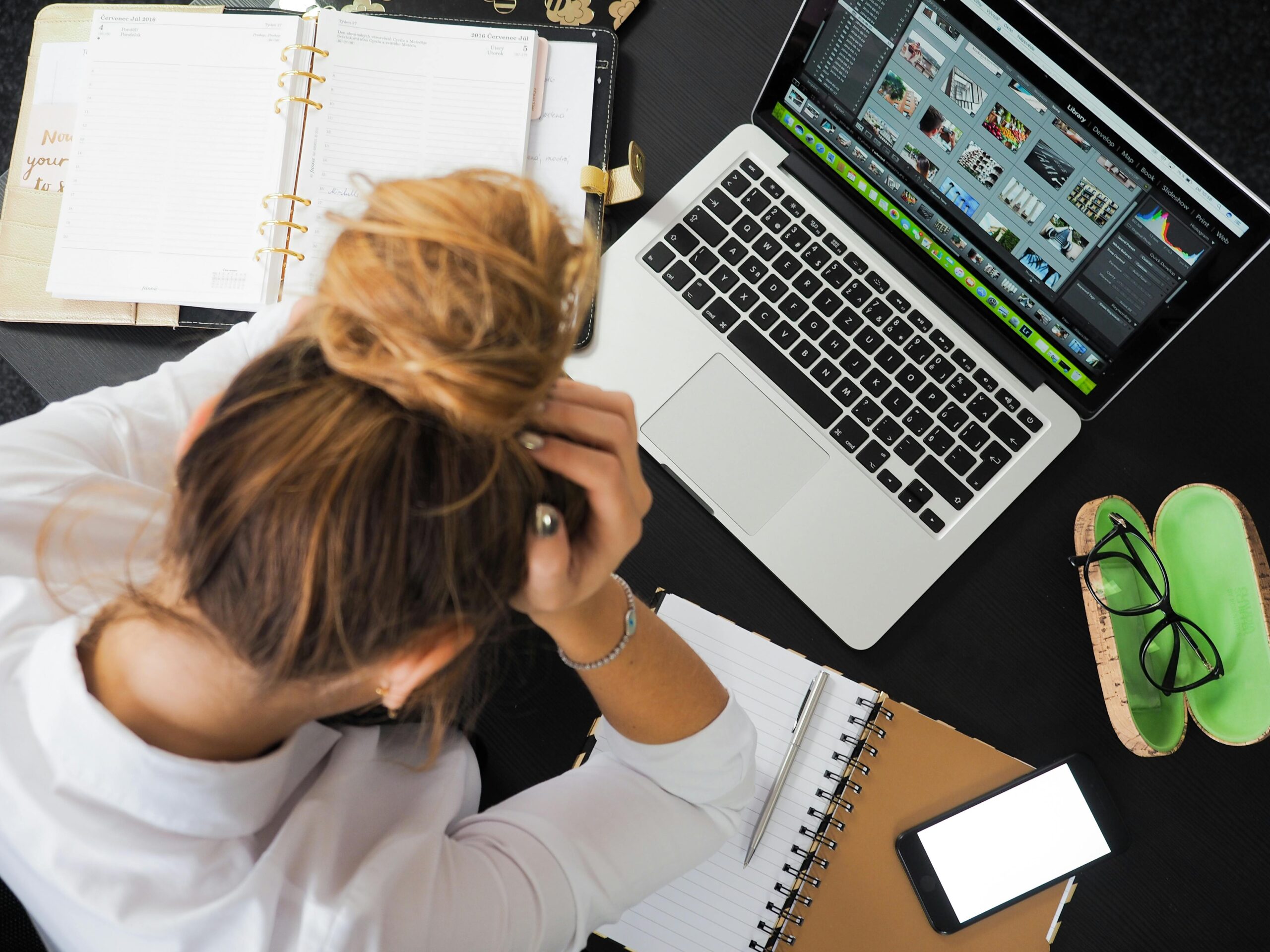 microsoft Azure Overhead view of a stressed woman working at a desk with a laptop, phone, and notebooks.